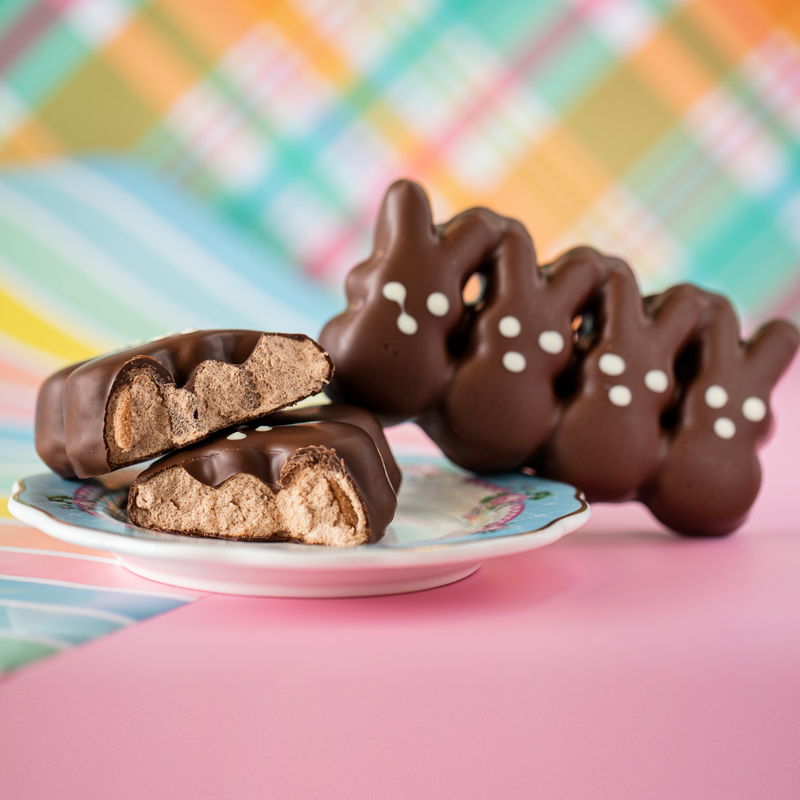 Chocolate covered candy with marshmallow chocolate bunnies on blue and orange plaid and pink background.